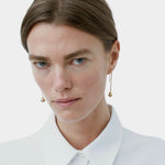 Model wearing long gold droplet earrings by RAGBAG Studio with a white collared shirt