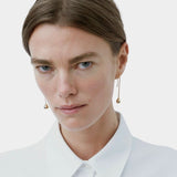 Model wearing long gold droplet earrings by RAGBAG Studio with a white collared shirt